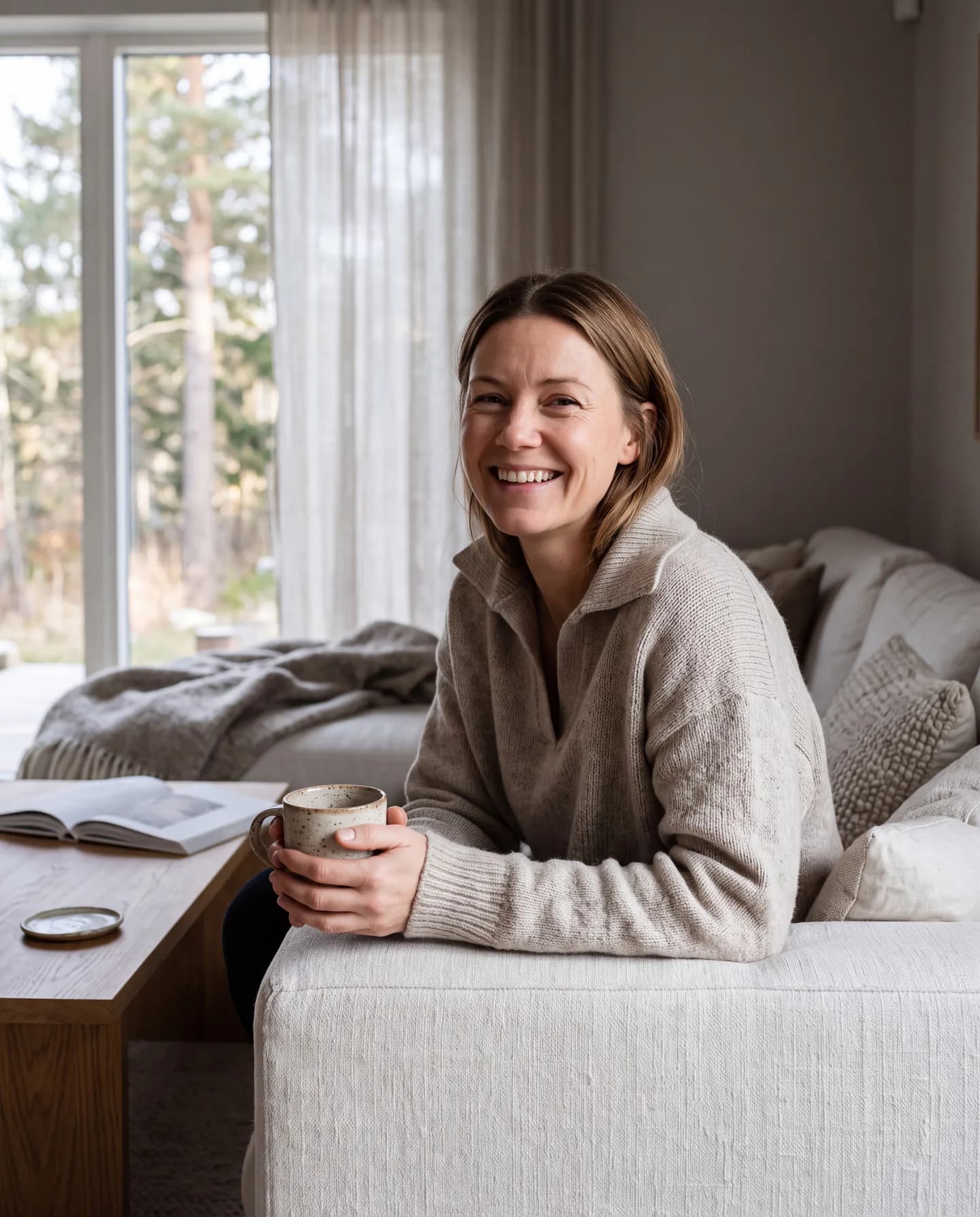 Illustration: en skrattande kvinna i stickad tröja sitter i soffan hemma med en kaffekopp.