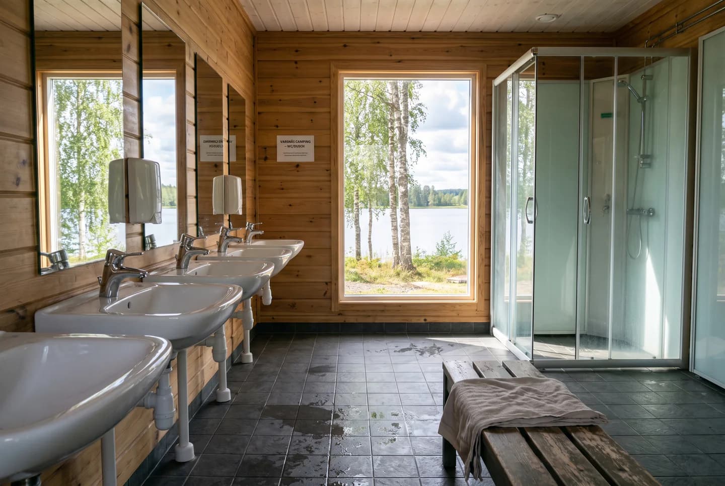 Illustration: servicehuset på en camping vid en sjö, med rena handfat, speglar och duschar.